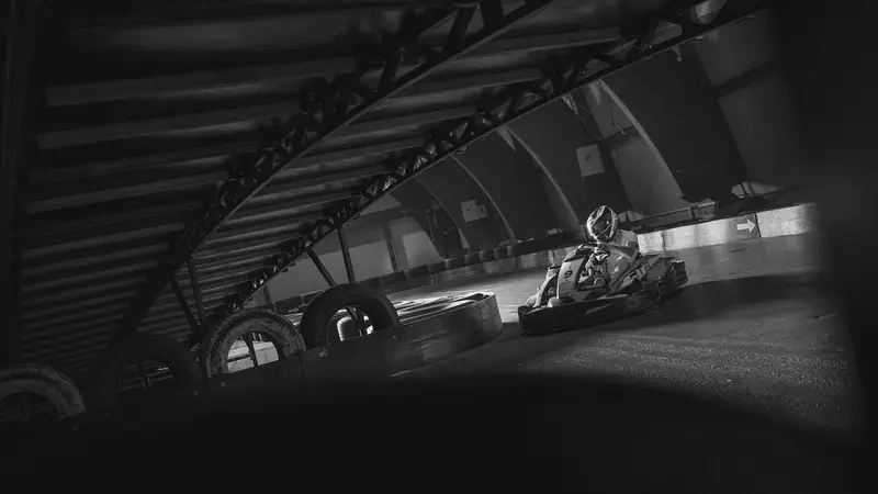 Kart in einer dunklen Indoorhalle unter Stahlbögen, am Rand der Strecke Reifenstapel