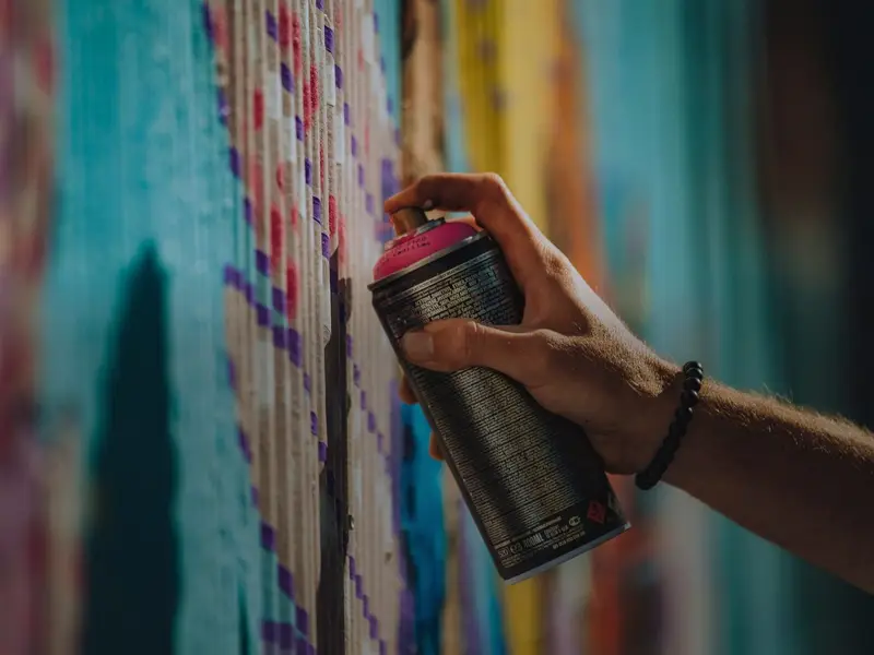 Hand mit einer magentafarbenen Spraydose vor einer bemalten Wand